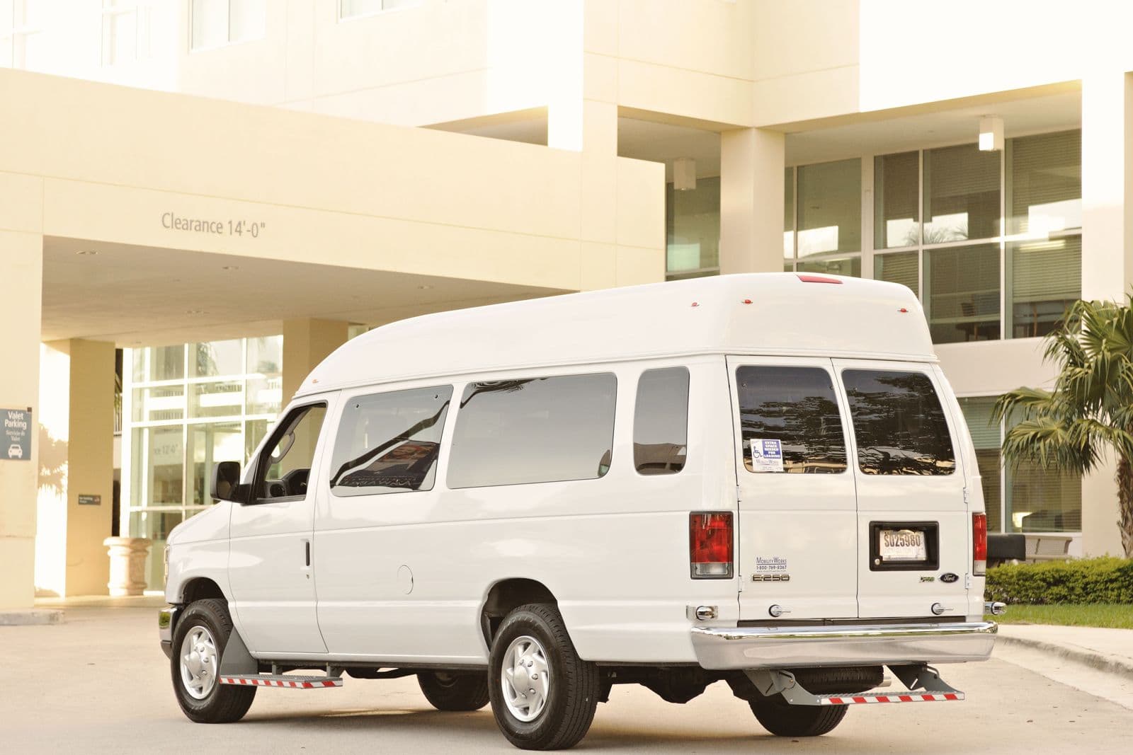 White passenger van parked outside a modern building under a clearance sign.
